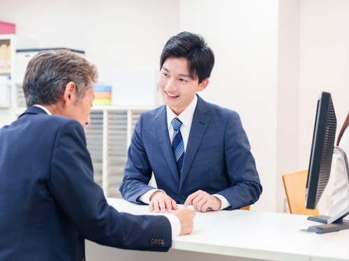 年配のスーツを着た男性とカウンター越しに会話する若いビジネスマン