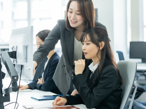 新入社員の座席でモニターを指しながら指導する先輩社員